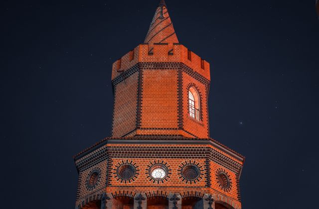 This photo captures the timeless beauty of a historic red brick tower, highlighted against a moonlit night sky. The architectural details, such as arched windows and gothic accents, evoke a sense of nostalgia and majesty. This image is ideal for use in travel brochures, history-themed blogs, or educational materials on architectural heritage.