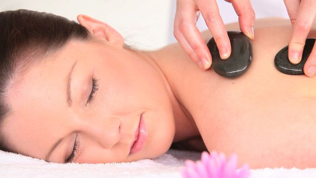 Woman is lying on a white towel during a hot stone massage at a spa. This serene scene depicts relaxation and wellness, making it perfect for advertisements and articles related to spa treatments, wellness tips, self-care, and relaxation techniques.