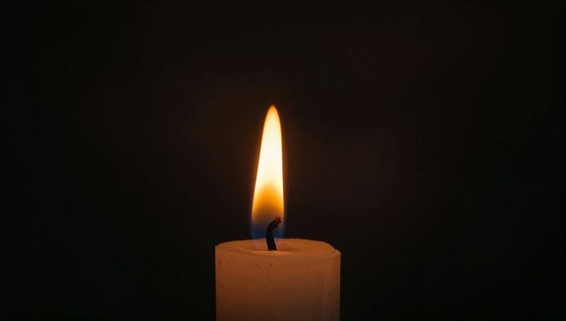 White candle burning with blue and amber flame casting soft halo