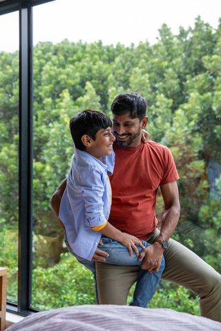 Happy father and son bonding by large glass window at home