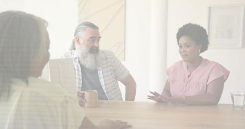 Woman speaking and gesturing during team discussion around table with laptop and mug