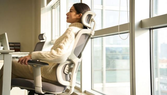 Woman reclining in ergonomic office chair near window in calm minimalist daylight workspace