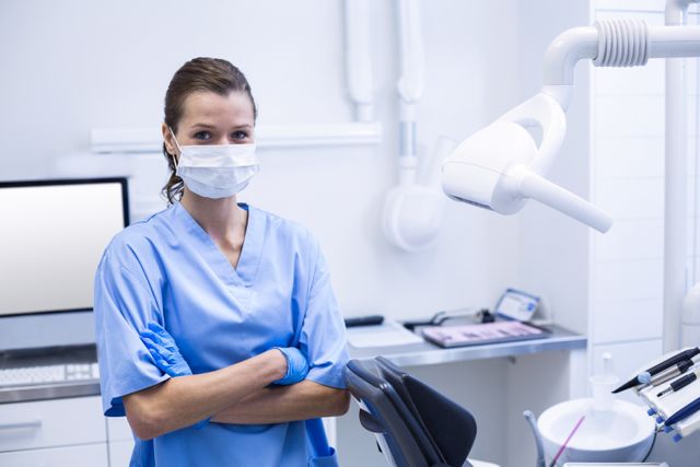 Dental assistant standing confidently in a modern dental clinic, wearing a mask and gloves. Ideal for use in healthcare promotions, dental clinic advertisements, medical training materials, and articles about dental care.