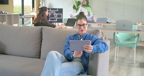 Diverse female coworkers collaborating in modern lounge using tablet, planning designs