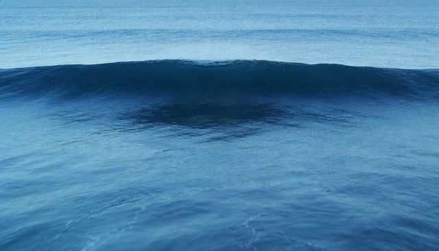 Rolling ocean wave cresting over deep blue swell with calm ripples and serene open sea horizon