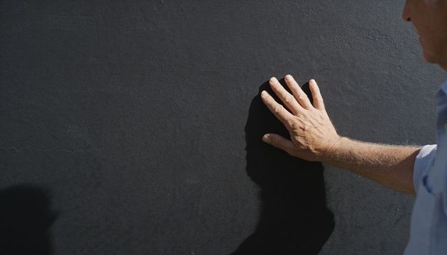 Sunlit hand touching textured black wall casting sharp shadow with copy space