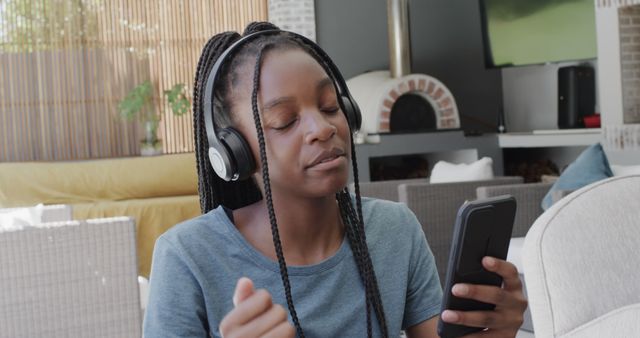 Young woman enjoying music through headphones while holding a smartphone. Ideal for content related to modern technology, leisure activities, and lifestyle. Great for promoting music streaming services, headphones, or smartphone apps.