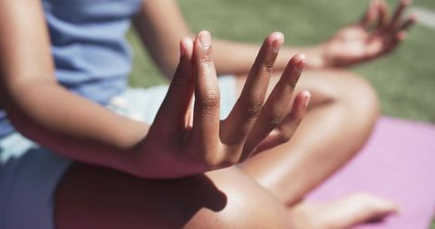 Sunlit teen sitting cross-legged meditating on purple yoga mat outdoors for mindfulness