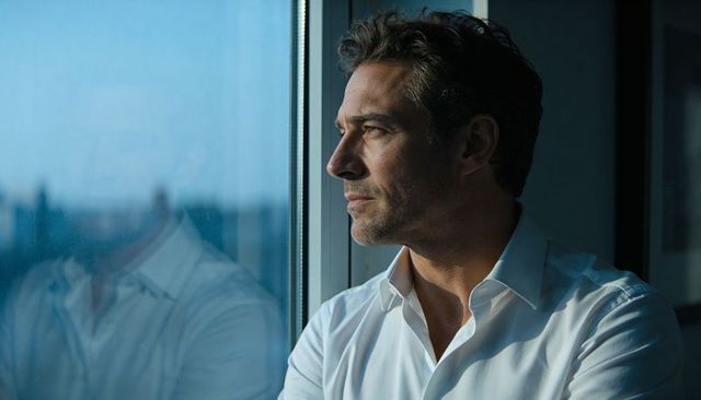 Executive gazing out office window at city skyline at dusk, reflective profile portrait