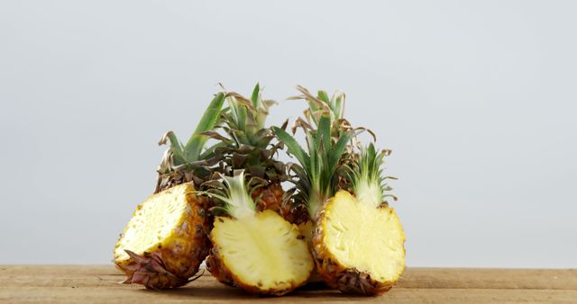 Two fresh pineapple halves placed on a wooden surface. Their juicy and vibrant yellow flesh contrasts against the rustic wood background, making this ideal for illustrating concepts of healthy eating, organic fruits, summer refreshments, recipes, or tropical themes in commercials and publishing.