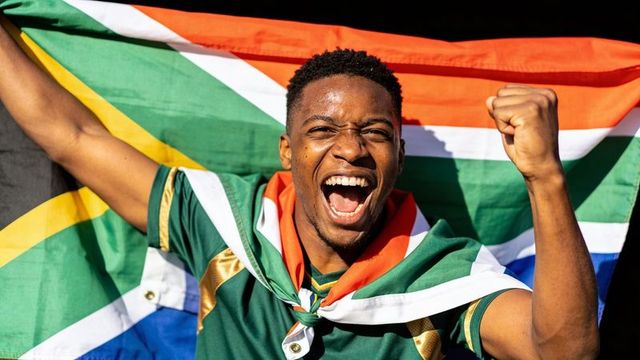 Young fan cheering while waving south african flag and raising fist in stadium celebration