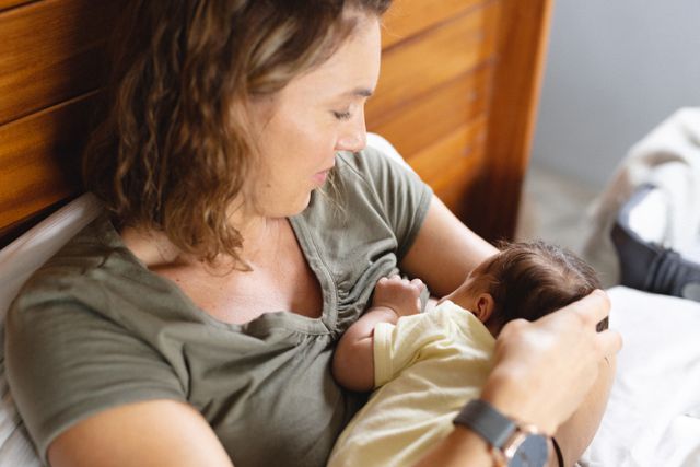 Mid adult caucasian mother breastfeeding newborn baby in bedroom at home. Ideal for use in parenting blogs, family care articles, and advertisements promoting maternal health and baby products.