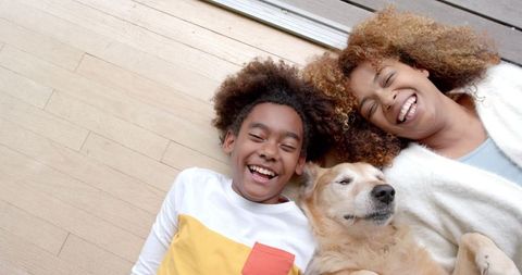Mother and son smiling with golden retriever on wooden floor