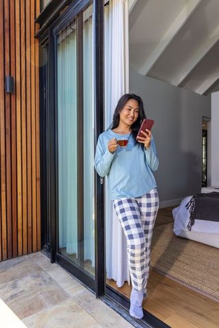Asian woman relaxing with tea and smartphone in sliding glass doorway morning routine