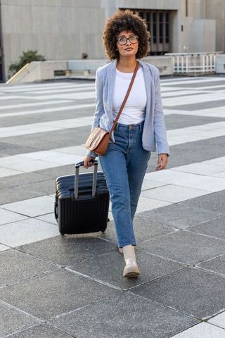 Urban professional woman walking with rolling suitcase across city plaza business travel
