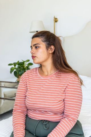 African american woman sitting on bed in cozy minimalist bedroom, looking thoughtful, calm