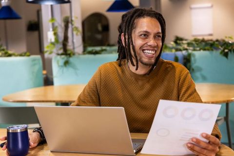 African American man smiling while working in coworking lounge with laptop and report