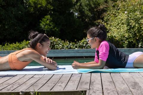 African american woman and girl sunbathing and chatting on pool dock, summer relaxation