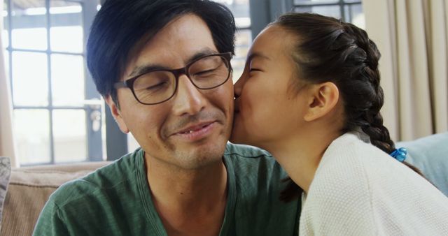 An Asian girl is giving a kiss on the cheek to a middle-aged Asian man, expressing affection and family love. Their warm interaction captures a tender moment of parental love and child's adoration.