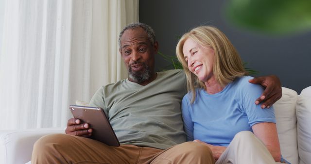 Biracial senior couple using digital tablet while sitting on the couch at home. staying at home in self isolation in quarantine lockdown