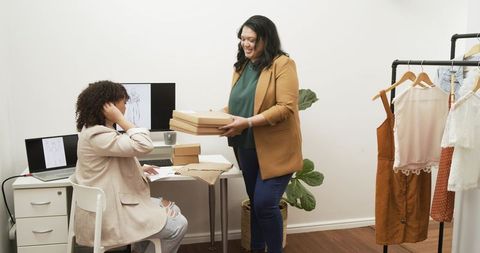 Diverse women packing and reviewing orders in boutique fashion studio, startup fulfillment