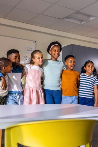 Smiling multiracial elementary students standing arm in arm in colorful classroom