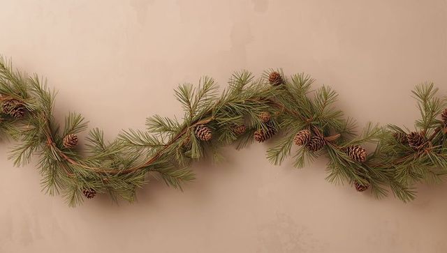 Minimal pine cone garland draping across warm beige wall with natural evergreen needles