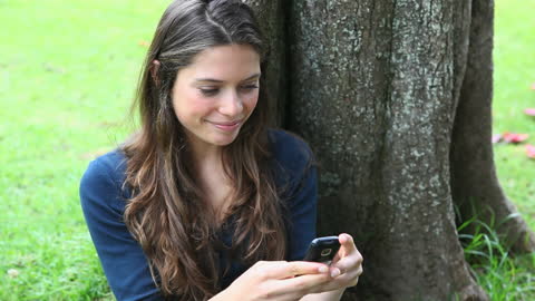 Relaxed Woman Smiling While Texting Beside Tree