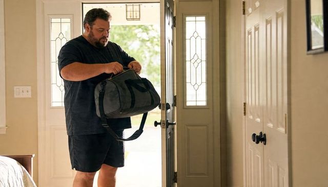 Man with duffel bag at front door preparing quick weekend trip for casual travel