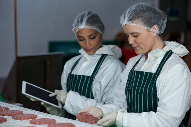 Female butchers maintaining records over digital tablet at meat factory
