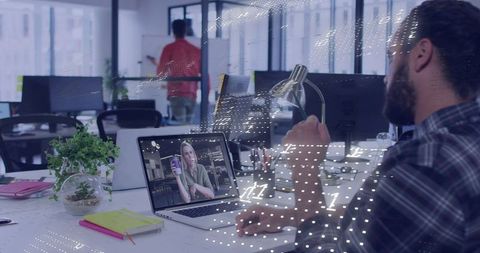 Bearded man video conferencing with colleague while working at modern open office desk