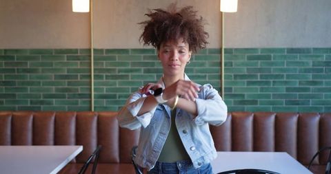 Young woman adjusting smartwatch while standing in cozy cafe with green tile wall