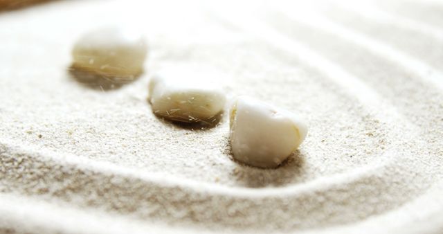 Zen-like arrangement of smooth white stones on fine sand creating tranquil patterns. Perfect for use in designs related to peace, mindfulness, and simplicity. Suitable for backgrounds in wellness, meditation, and relaxation themes.
