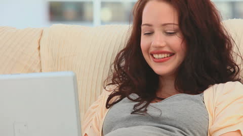 Pregnant Woman Smiling While Using Her Laptop at Home