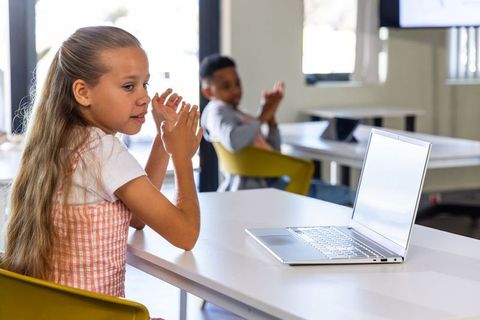 Elementary students applauding during digital lesson with laptop in bright classroom