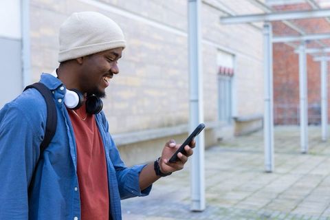 Smiling african american student checking smartphone on campus courtyard with headphones