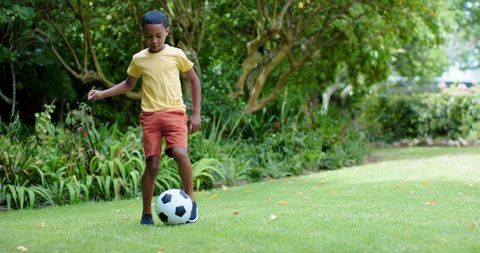 African american boy dribbling soccer ball on sunny backyard lawn outdoor kids sports