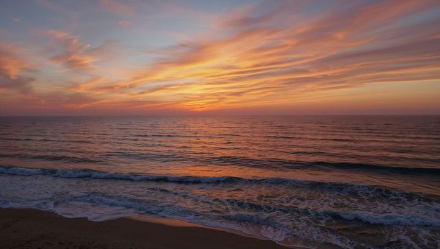 Glowing sunset sky casting warm reflections across calm ocean and sandy shoreline