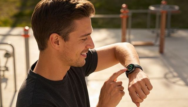 Smiling man checking fitness smartwatch during outdoor gym workout at sunny urban park