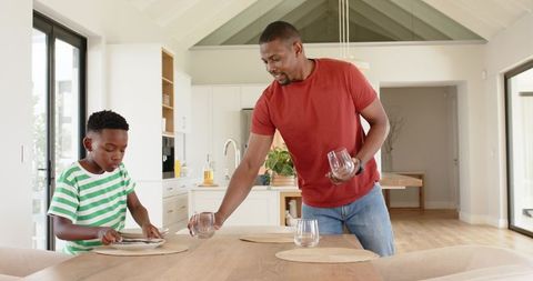 African-American father and son placing tableware in modern open-plan kitchen