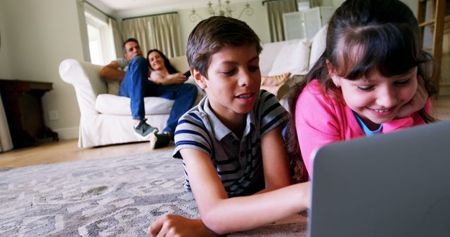 Two children are playing on a laptop on the rug in a cosy living room while their parents relax on a couch in the background. This scene depicts a loving family spending quality time together indoors. Ideal for use in family-oriented content, technology in education discussions, or advertisements promoting family bonding and digital devices.