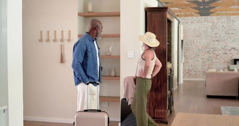 Senior couple preparing for trip in modern entryway with luggage and straw hat