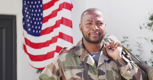 Portrait of happy african american male soldier holding bag with flag of usa in the background. Patriotism, army and returning home concept.