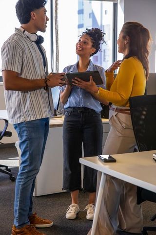 Diverse coworkers collaborating with tablet in bright open-plan office, casual teamwork
