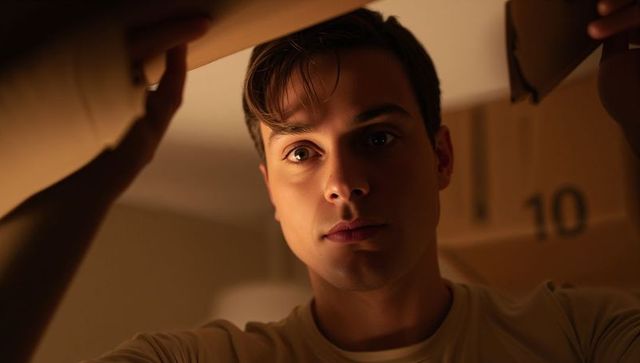 Young man peering inside moving box holding flaps while unpacking at home