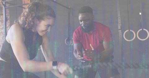 Woman pedaling on air bike while coach guiding intense cardio training and motivation