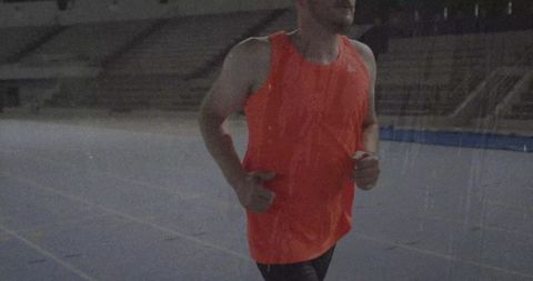 Athlete Running on Track in Empty Stadium in Orange Gear
