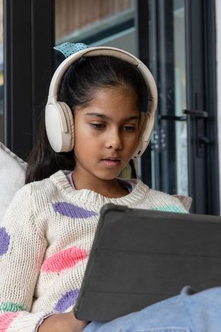 Indian preteen girl studying on tablet wearing headphones for remote learning in knit sweater