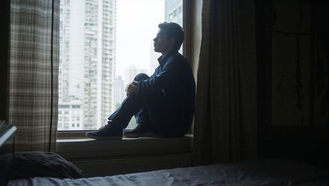 Man sitting on window ledge contemplating city skyline in moody urban interior