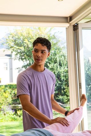 Therapist assisting client with leg stretch in sunny treatment room